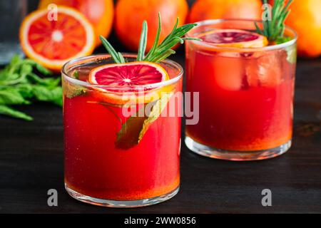 Sparkling Blood Orange Mocktails Garnished with Fresh Herbs: Mocktails with citrus juice, ginger, turmeric, rosemary, and mint in rocks glasses Stock Photo