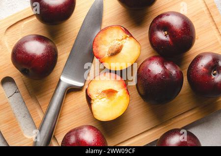 Ripe plums on wooden cutting board and knife on grey background. Stock Photo