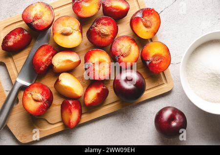 Fresh plums on cutting board with knife and sugar on grey background. Stock Photo