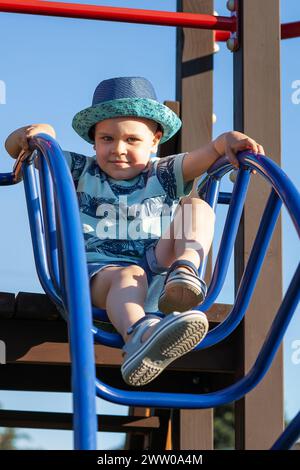 Little boy climbs up the ladder on the playground. child climbs confidently up the ladder against the blue sky. Stock Photo