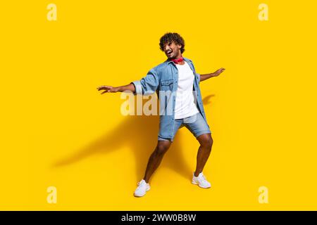 Full size photo of nice young male surfing have fun wear trendy denim outfit red scarf isolated on yellow color background Stock Photo