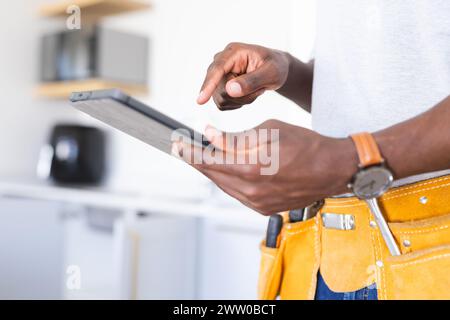 African American workman in tool belt interacts with a tablet Stock Photo
