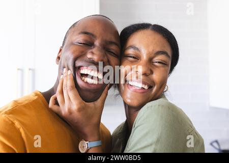 A joyful African American couple is sharing a laugh together at home in the kitchen Stock Photo