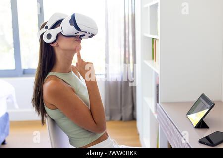 A young Caucasian woman is immersed in virtual reality, using a headset at home Stock Photo