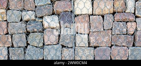 View of a pebble stone wall held in place with a wire retainer. Panoramic photo. Stock Photo