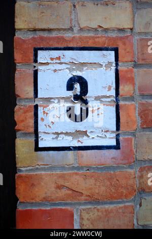 Painted house number three. The paint is peeling a bit. Seen in Bruges, Belgium Stock Photo