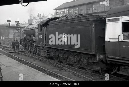 1950s, historical, Briitsh Railways steam locomotive, 60112 on the rail track , coal wagon full, sitting in station, England, UK, guard and driver walking across track. Built for the GNR, the A3 Class Gresley designed locomotive was introduced in 1923, transfering to LNER the following year and later onto the new British Railways in 1948. Stock Photo