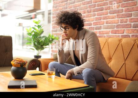 Pensive young man sitting in a cafe with a glass of whiskey Stock Photo