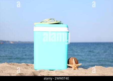 Modern beach cooler, flip-flops, starfish and coconut on sand Stock Photo