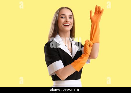 Portrait of female janitor putting on rubber gloves against yellow background Stock Photo