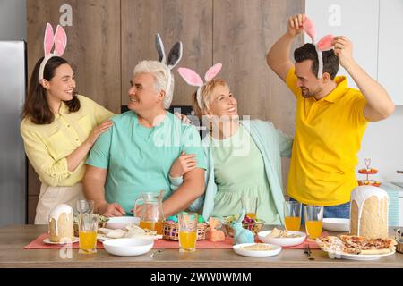 Happy family with bunny ears at Easter dinner in kitchen Stock Photo