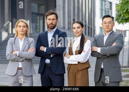 Four professional business individuals posing confidently outdoors, displaying teamwork and corporate success in a modern urban setting. Stock Photo