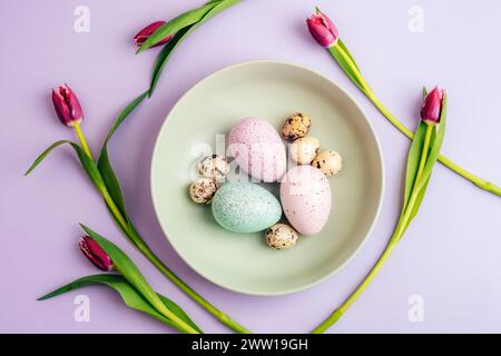 Easter table setting with green plate, purple tulips and Easter eggs on lilac background. Top view, flat lay. Stock Photo