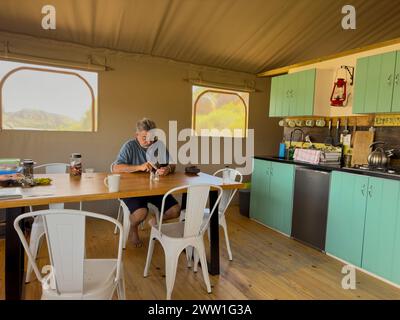 Vleiplaas Clanwiliam Cederberg South Africa. 14/02/2024.  A male camper using a mobile phone inside the dining area of a large tent. Stock Photo