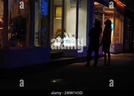 Two women stop along the sidewalk t window shop at night at the chic and luxury stores in East Hamptons, part of the Hamptons Stock Photo