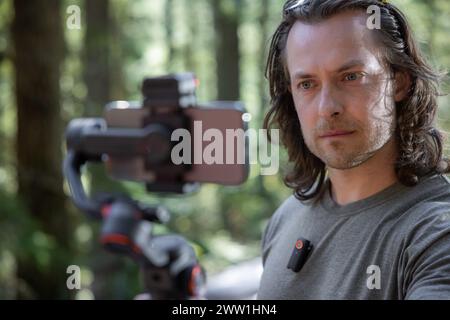 Content creator using. a phone gimbal to film in nature with a blurred forest in the background Stock Photo