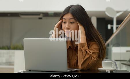 Exhausted overworked Asian chinese japanese woman student girl studying online with laptop in cafe tired sick businesswoman think difficult decision Stock Photo