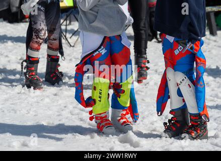 Massachusetts Interscholastic Athletic Association (MIAA) 2024 High School Alpine skiing annual state championship Slalom and Giant Slalom at Wachusett Mountain ski area in Princeton, MA. More than 300 students competed in the championships.  Two female racers wearing race suits, protective padding and ski boots talking between races. Stock Photo