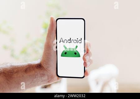 Android logo on mobile phone screen. Man holding a smartphone showing the new Android logo 2023. Stock Photo
