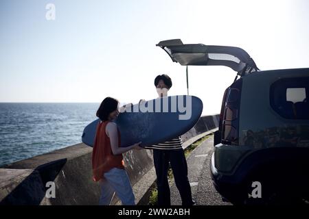 A man and a woman standing next to a car with a surfboard Stock Photo