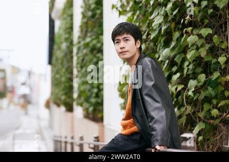 A man in an orange jacket and black pants leaning against a railing Stock Photo