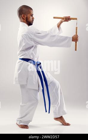 Karate, fight and man with nunchaku in martial arts, studio or training with weapon for defence on white background. Nunchucks, exercise and fighting Stock Photo