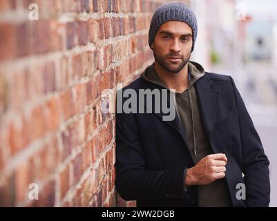 Man, portrait and urban style by brick wall downtown for aesthetic, modern and vacation for city culture. Male person, trendy winter outfit for Stock Photo