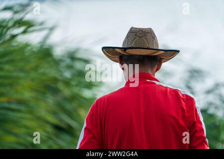 Old man with red jacket and light brown cowboy hat with black ornament design. Green reeds and sky , as blurry background. Fisherman story. Stock Photo