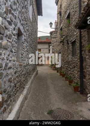 A narrow alley with a stone wall on either side. The street is lined with potted plants and has a cobblestone path. Medieval and ancient streets. Stock Photo