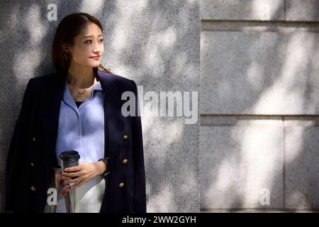 A woman in a blue shirt and jacket leaning against a wall Stock Photo