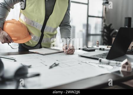 Engineering hold safety helmet working with drawings inspection on the office desk. Engineer, Architect, Industry and factory concept. Stock Photo