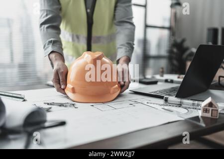 Engineering holding safety helmet with drawings inspection on the office desk. Engineer, Architect, Industry and factory concept. Stock Photo