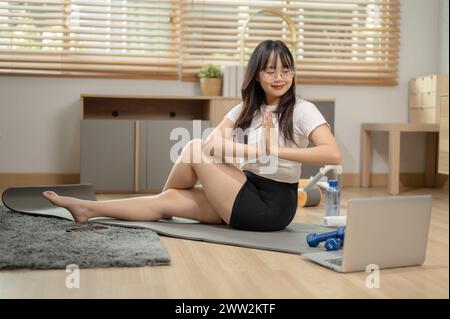 A happy, positive young Asian woman is practicing yoga at home, watching the yoga tutorial video online. people and domestic life concepts Stock Photo