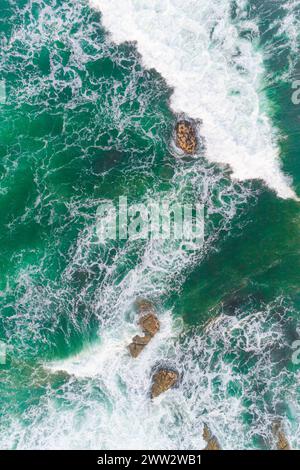 Aerial drone top down bird eye view of sea green waves break on rocks Stock Photo