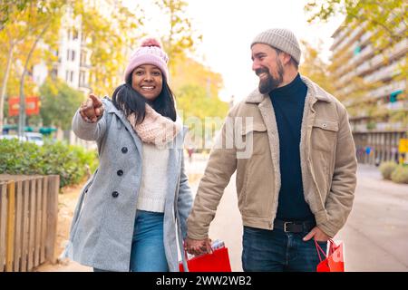 Happy friends or couple walking, pointing at smart hotel location outdoors. Stock Photo