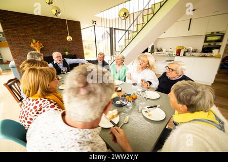 A lively family gathering around a dinner table, immersed in conversation within a modern home. The scene is set with a spacious kitchen backdrop, large windows, and an elegant staircase, adding a touch of sophistication to the familys mealtime. Cheerful Family Dinner in Modern Home with Conversations. High quality photo Stock Photo