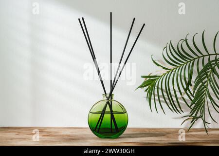 Aromatic Reed Diffuser on Wooden Table With Vibrant Green Leaves Against White Background Stock Photo