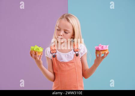 Studio, girl and choice with cupcakes, dessert and decision for snack and childhood. Child, sweets and yummy selection for tasty, eating and choosing Stock Photo