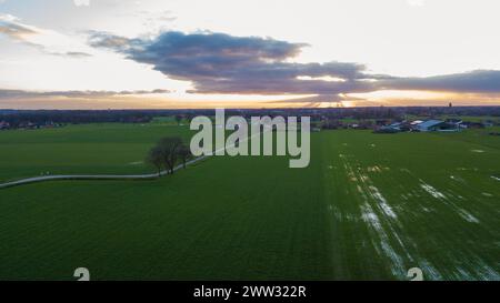 The evening sky graces a rural setting with sunbeams piercing through clouds, casting dramatic shadows over the green fields. This aerial shot captures the quiet beauty of the countryside as night approaches. Aerial View of Sunbeams Breaking Through Clouds Above Rural Landscape. High quality photo Stock Photo