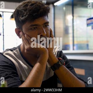 A thoughtful young man sits alone at a cafe table, lost in thought Stock Photo