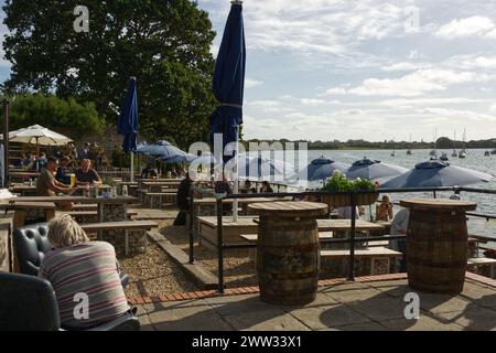 People enjoying food and drink on the waterfront terrace of the Crown and Anchor pub at Dell Quay in Chichester Harbour, West Sussex, England Stock Photo
