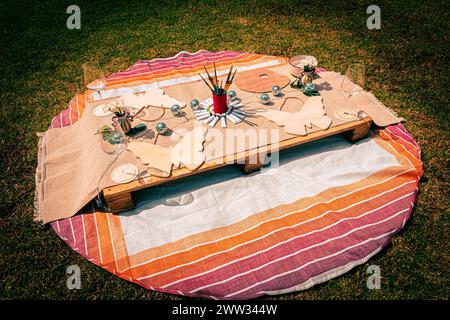 Top-down shot of a bohemian picnic set up with art and dining essentials on grass. Stock Photo