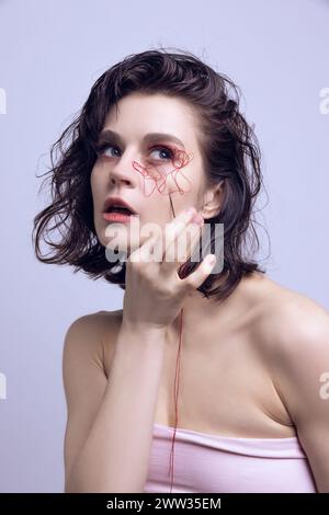 Portrait of beautiful woman with red string on face and hand with needle. Complexities of beauty, facial changes. Stock Photo