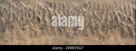 Abstract structure in the brown sand on the beach at low tide, below with shallow water Stock Photo