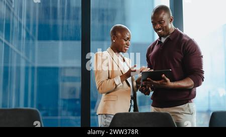 Two professional colleagues, a man and a woman, are engaged in a discussion while reviewing information on a digital tablet. They demonstrate teamwork Stock Photo
