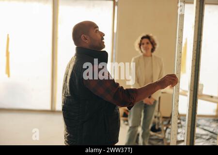 Mature male construction worker discussing his suggestions for a home renovation project with an architect. He stands inside a house, examining a door Stock Photo