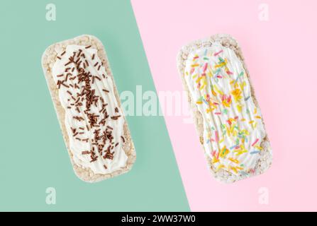 Two oblong rice cakes topped with soft cheese, chocolate and colored sprinklers on duo colored background Stock Photo