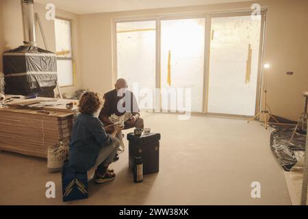 Happy couple taking a break from their home renovation DIY work, enjoying a snack and chatting together. Mature husband and wife working as a team, de Stock Photo