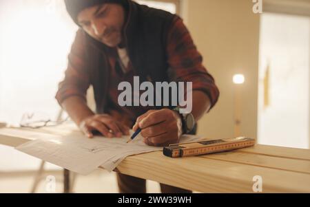 Professional remodeler marks blueprints amidst a home renovation project. Man working on redesigning a kitchen interior. Carpentry work with wood plan Stock Photo
