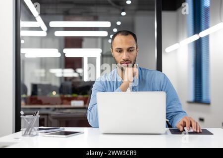 Focused professional using a laptop at an organized workspace with modern design in a corporate office. Stock Photo
